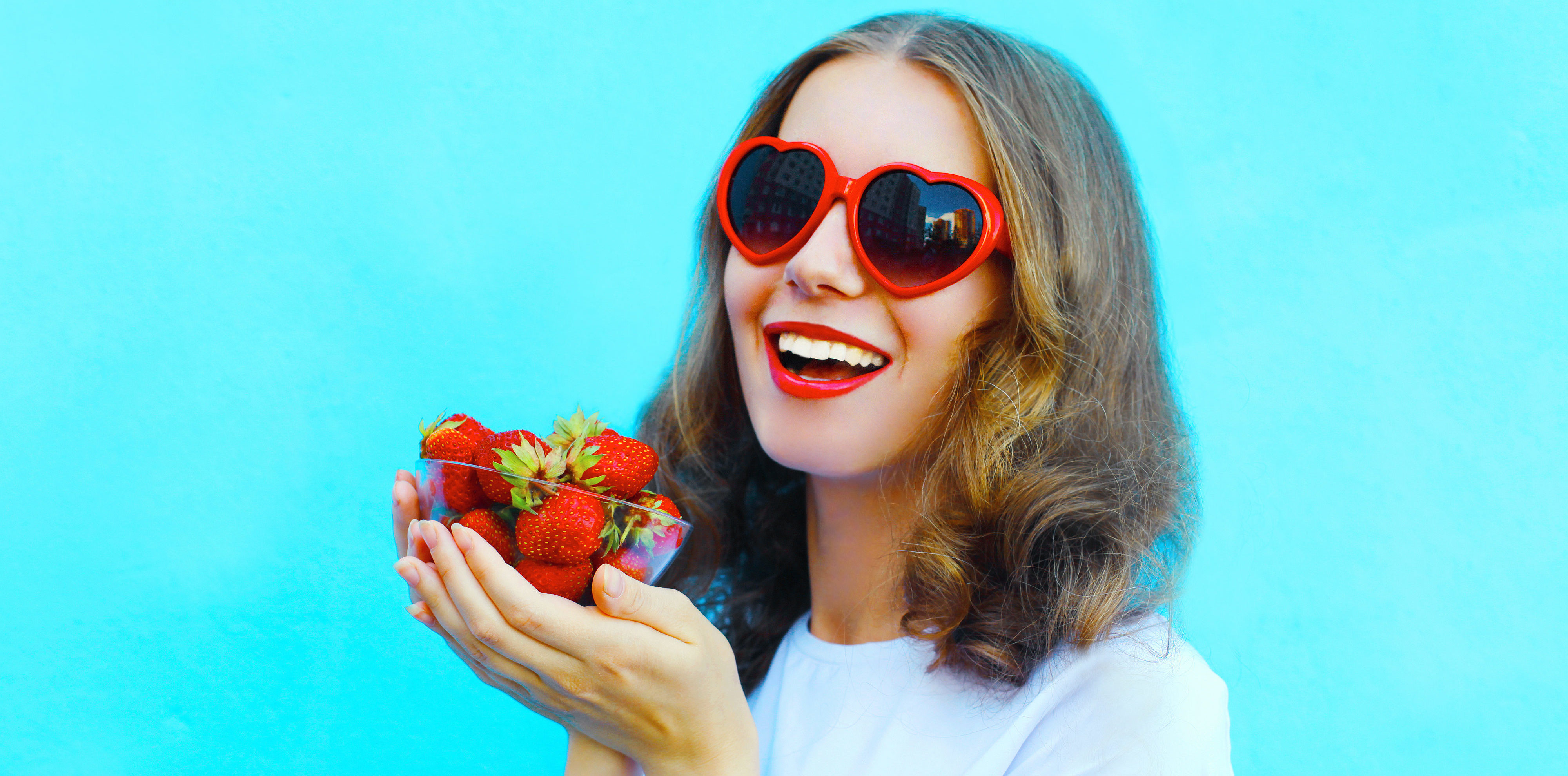 Happy smiling woman with many strawberry over colorful blue back kursy języka polskiego dla obcokrajowców